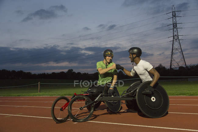 Athlètes paraplégiques poing cognant sur la piste de sport, entraînement pour la course en fauteuil roulant la nuit — Photo de stock