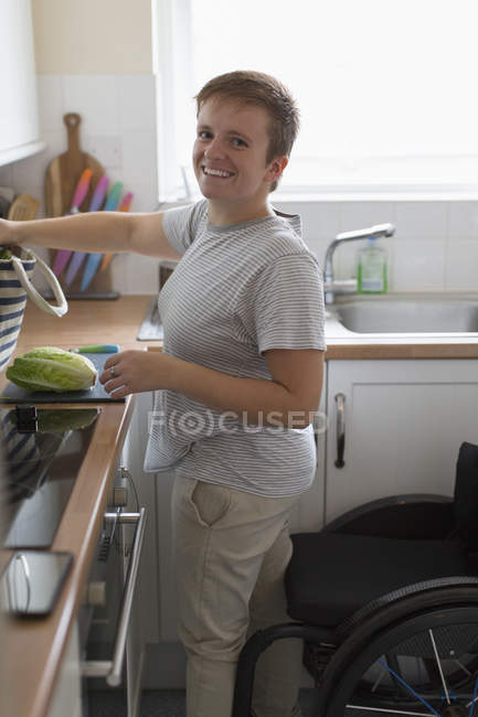 Portrait smiling young woman with wheelchair cooking in apartment kitchen — Stock Photo
