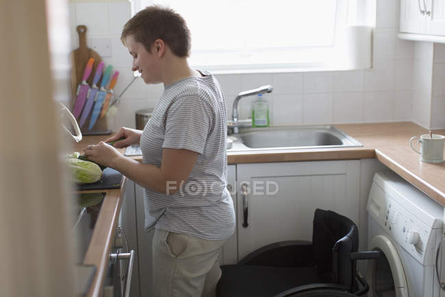 Женщина с инвалидной коляской режет овощи на кухне квартиры — стоковое фото