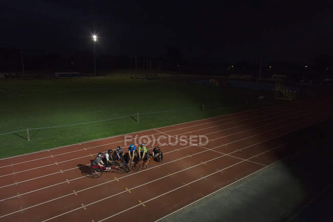 Athlètes paraplégiques sur piste de sport, entraînement pour course en fauteuil roulant la nuit — Photo de stock