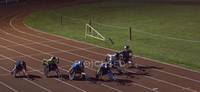 Athlètes paraplégiques accélérant le long de la piste de sport en course en fauteuil roulant la nuit — Photo de stock