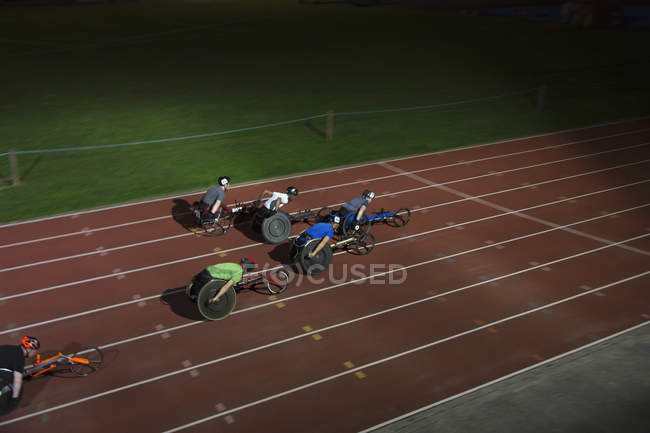 Athlètes paraplégiques accélérant le long de la piste de sport en course en fauteuil roulant la nuit — Photo de stock