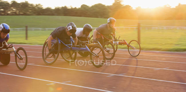 Atletas paraplégicos determinados acelerando ao longo da pista de esportes em corrida em cadeira de rodas — Fotografia de Stock