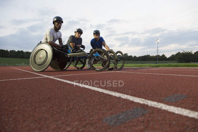 Retrato determinado atletas parapléjicos entrenamiento para la carrera en silla de ruedas en pista deportiva - foto de stock