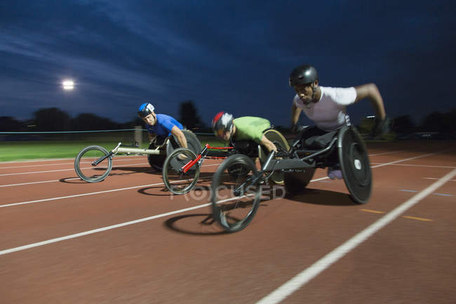 Паралитические спортсмены, гоняющиеся по спортивной трассе в гонке на инвалидных колясках ночью — стоковое фото