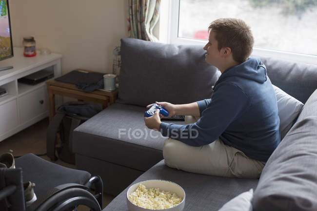 Молодая женщина играет в видеоигры на диване рядом с инвалидной коляской — стоковое фото