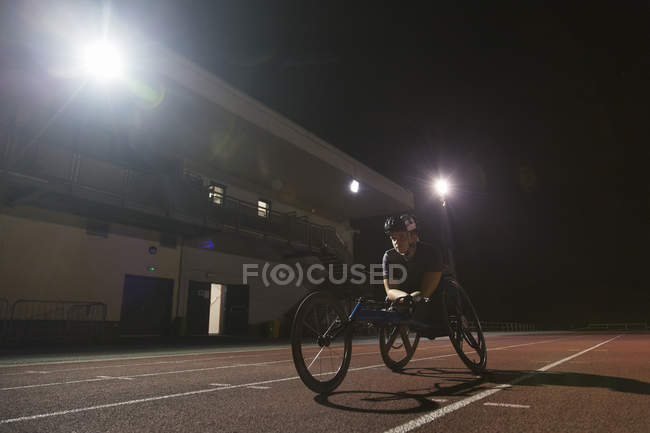 Treinamento de atleta paraplégico feminino determinado para corrida em cadeira de rodas em pista esportiva à noite — Fotografia de Stock