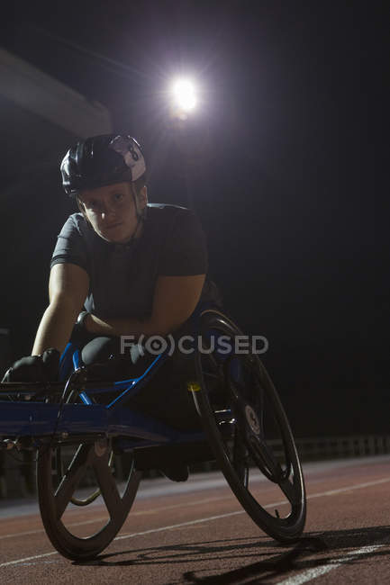 Retrato determinado jovem atleta paraplégico do sexo feminino treinamento para corrida em cadeira de rodas em pista de esportes à noite — Fotografia de Stock