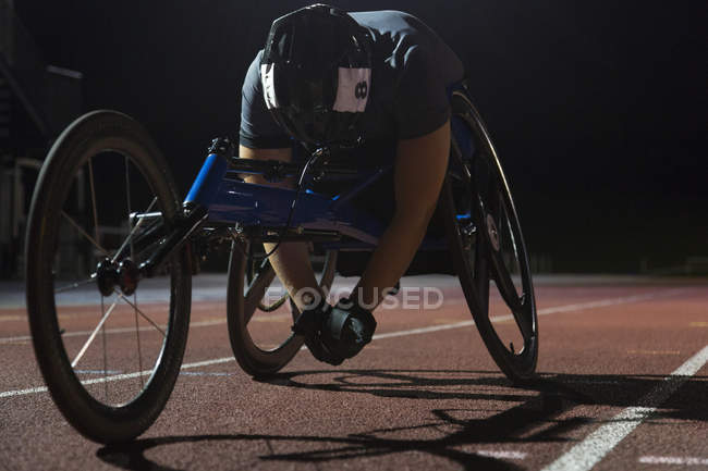 Atleta parapléjico cansado descansando en pista deportiva después de la carrera en silla de ruedas por la noche - foto de stock