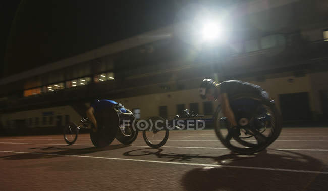 Paraplegic athletes speeding along sports track in wheelchair race at night — Stock Photo