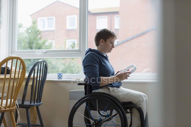 Junge Frau im Rollstuhl mit Kopfhörern am Fenster — Stockfoto