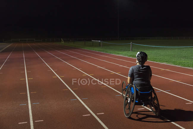 Entrenamiento de atleta parapléjico femenino determinado para la carrera en silla de ruedas en pista deportiva por la noche - foto de stock