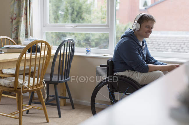 Jeune femme en fauteuil roulant écoutant de la musique avec écouteurs à la fenêtre — Photo de stock