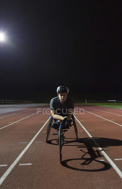 Retrato confiante atleta paraplégico no treinamento de pista de esportes para corrida em cadeira de rodas à noite — Fotografia de Stock