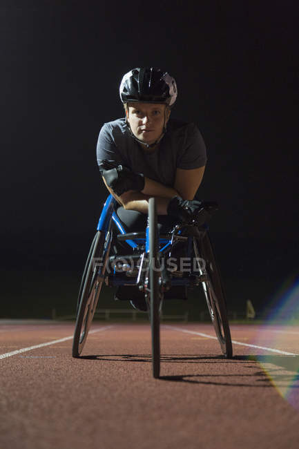 Retrato determinado, duro joven mujer atleta parapléjico entrenamiento para la carrera en silla de ruedas en pista deportiva por la noche - foto de stock
