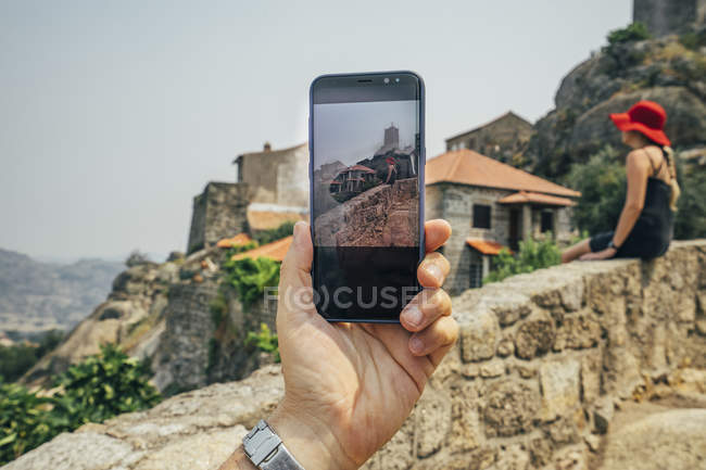 Perspective personnelle homme avec appareil photo téléphone photographie femme sur mur de pierre, Monsanto, Portugal — Photo de stock