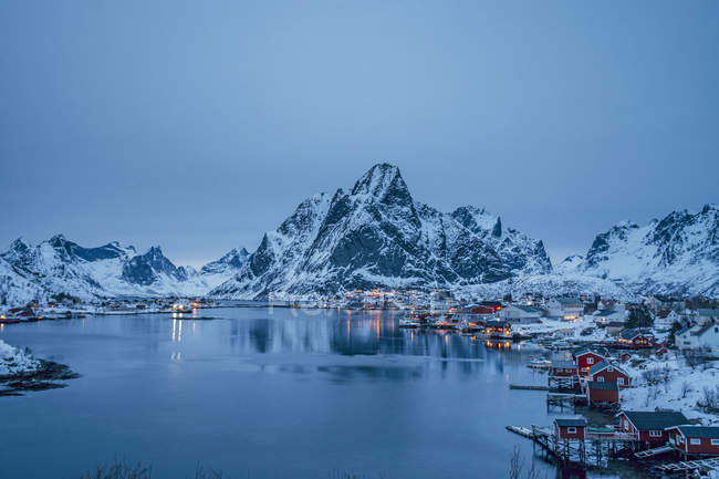 Vista tranquila da vila de pescadores à beira-mar coberta de neve e montanhas à noite, Reine, Lofoten Islands, Noruega — Fotografia de Stock