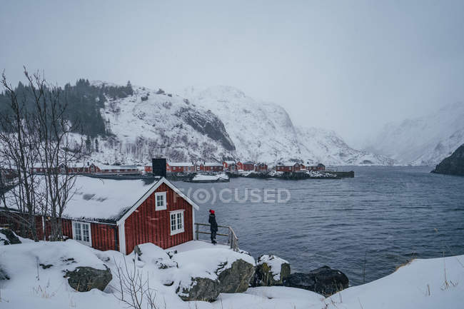 Mulher desfrutando de tranquila vista para a montanha nevada da vila de pescadores à beira-mar, Ilhas Lofoten, Noruega — Fotografia de Stock