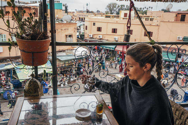 Femme dégustant du thé sur le balcon donnant sur le marché de la rue, Marrakech, Maroc — Photo de stock