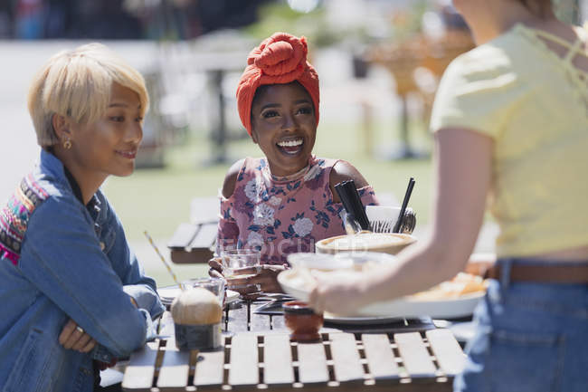 Молоді жінки друзі насолоджуються обідом в сонячному тротуарному кафе — стокове фото