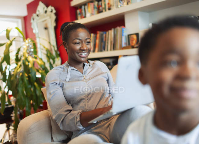 Mujer sonriente usando portátil en el sofá de la sala de estar - foto de stock