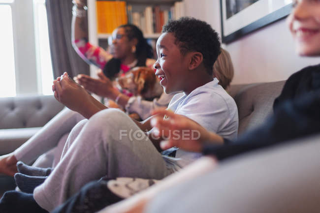 Niño entusiasta jugando videojuego con la familia en el sofá de la sala de estar - foto de stock