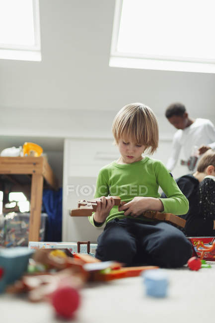 Любопытный мальчик собирает деревянные блоки на полу — стоковое фото