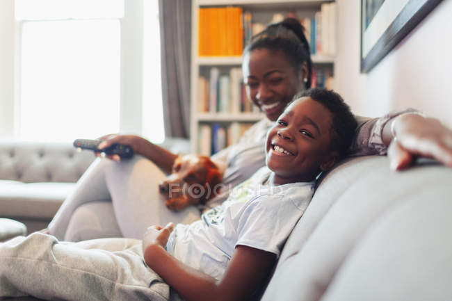 Portrait happy mother and son with dog watching TV on living room sofa — Stock Photo