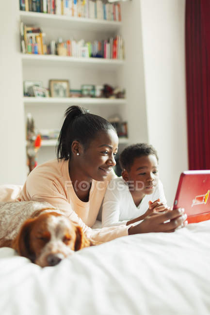 Perro durmiendo junto a madre e hijo usando tableta digital - foto de stock