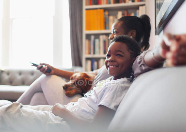 Happy boy watching TV with mother and dog on living room sofa — Stock Photo