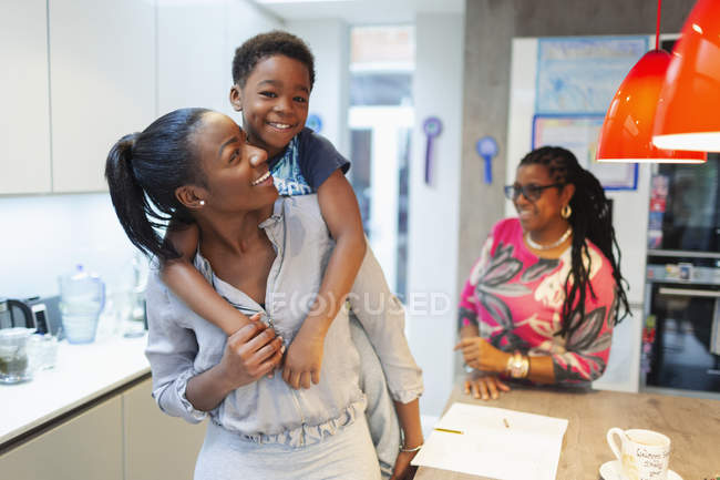 Portrait carefree mother and son piggybacking in kitchen — Stock Photo