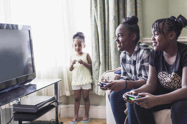 Kleinkind Mädchen beobachtet zwei Schwestern beim Videospiel im Wohnzimmer — Stockfoto