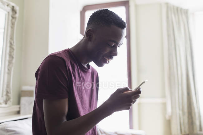 Sourire adolescent garçon textos avec téléphone intelligent — Photo de stock