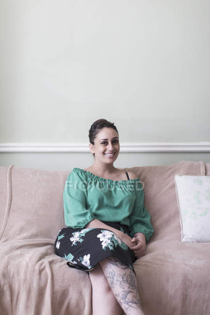 Portrait femme souriante et confiante avec des tatouages sur le canapé du salon — Photo de stock