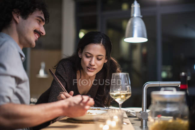 Couple eating dinner with chopsticks and drinking white wine in apartment kitchen — Stock Photo