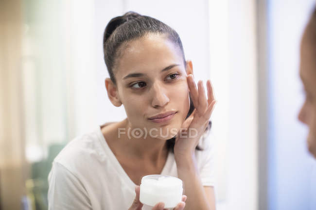 Donna che applica idratante al viso nello specchio del bagno — Foto stock