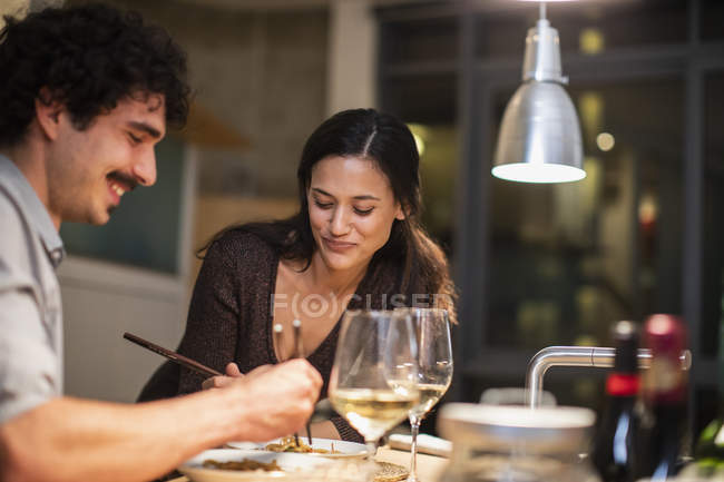 Couple eating with chopsticks and drinking white wine in apartment kitchen — Stock Photo