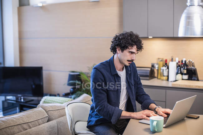 Homem trabalhando no laptop na cozinha do apartamento — Fotografia de Stock