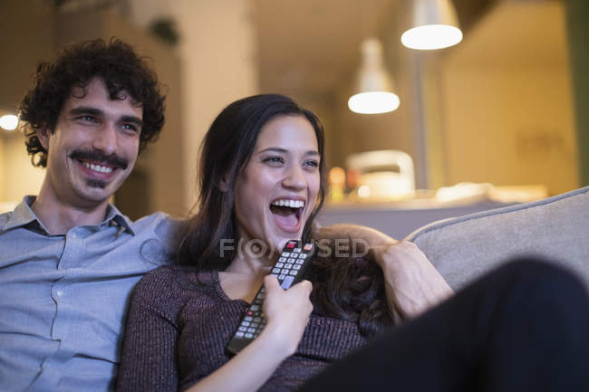 Casal rindo assistindo TV no sofá — Fotografia de Stock