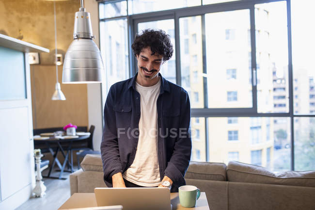 Uomo sorridente utilizzando il computer portatile in appartamento — Foto stock