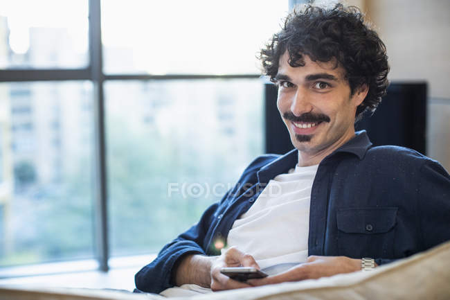 Портрет улыбающийся мужчина с помощью смартфона на диване — стоковое фото
