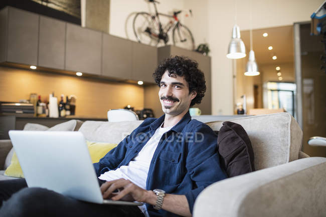 Retrato sorrindo homem usando laptop no sofá apartamento — Fotografia de Stock