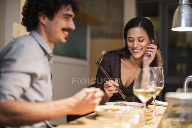 Happy couple eating dinner with chopsticks and drinking white wine — Stock Photo