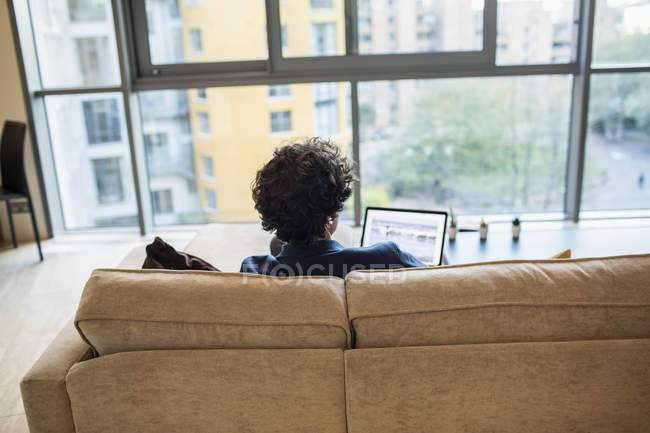 Hombre usando el portátil en el sofá del apartamento - foto de stock