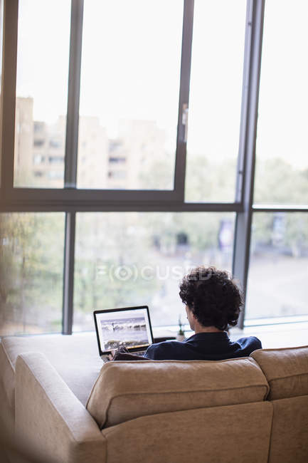 Homem usando laptop no sofá apartamento urbano — Fotografia de Stock