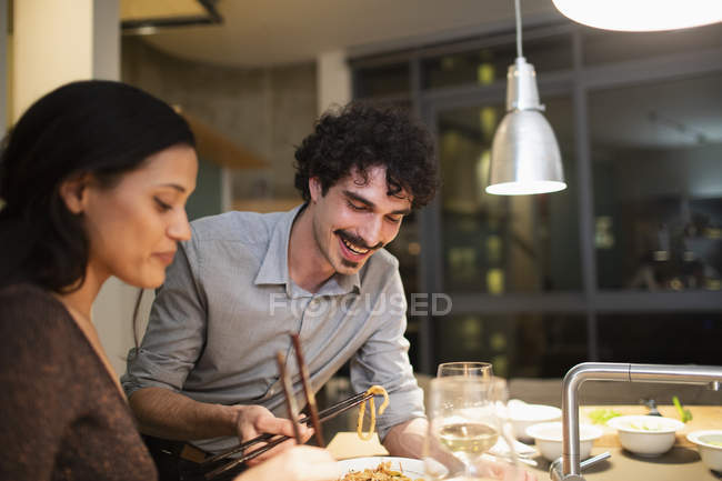 Pareja sonriente cenando con palillos en la cocina del apartamento - foto de stock