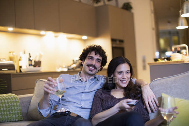 Happy couple drinking white wine and watching TV on apartment sofa — Stock Photo