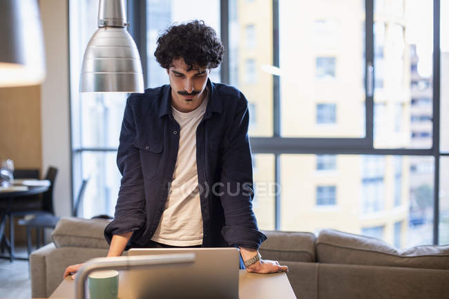 Man using laptop in urban apartment kitchen — Stock Photo