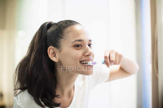 Mujer feliz cepillarse los dientes en el espejo del baño - foto de stock