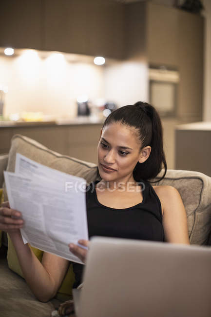 Mulher lendo papelada no laptop no sofá — Fotografia de Stock